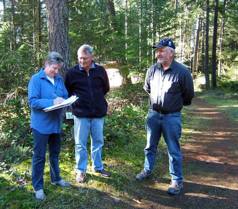 Three people stand on a trail. One is signing papers