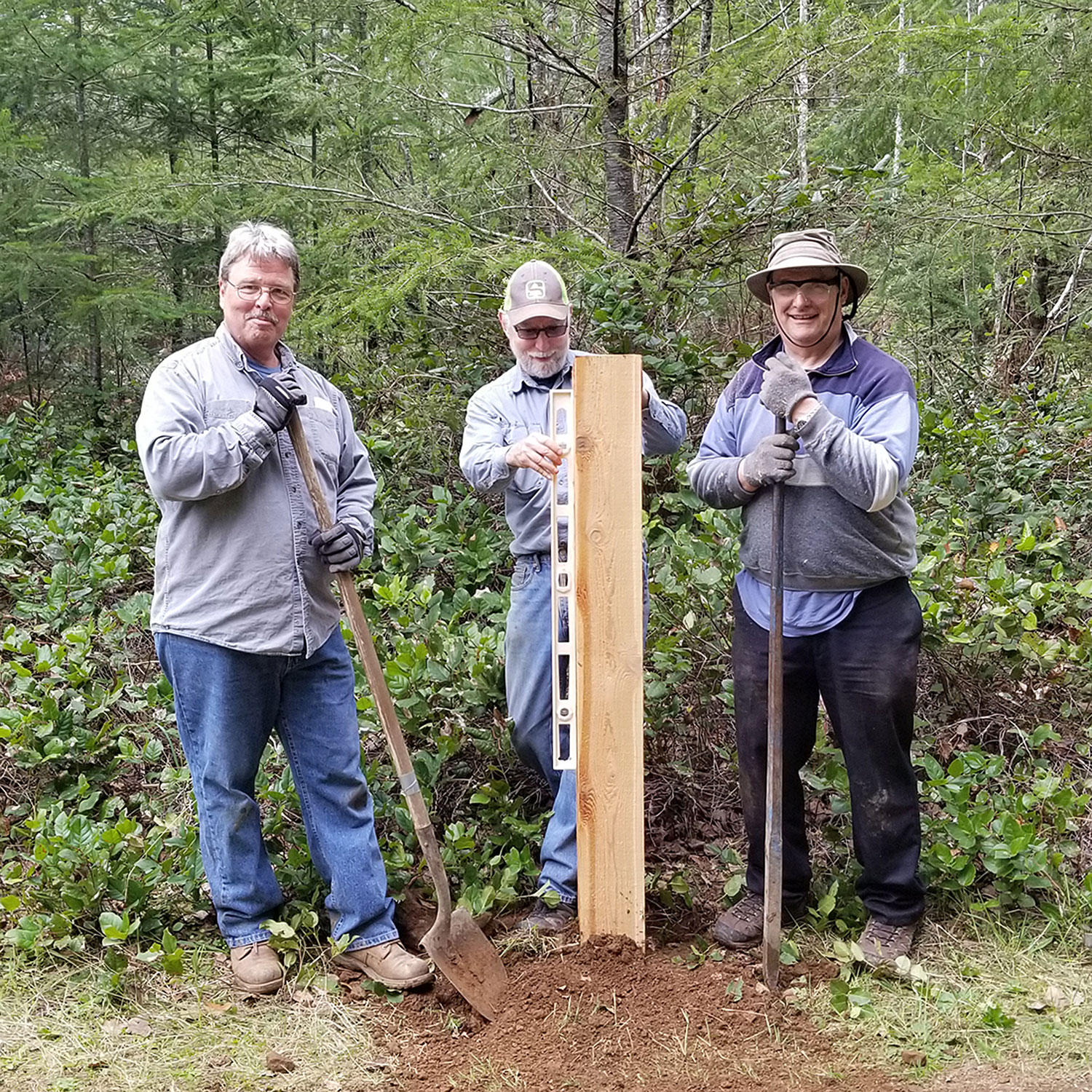 Men standing with a new trail signpost; middle man is leveling it.