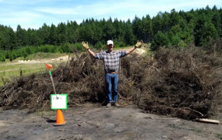 Person gesturing proudly in front of a big pile of broom.