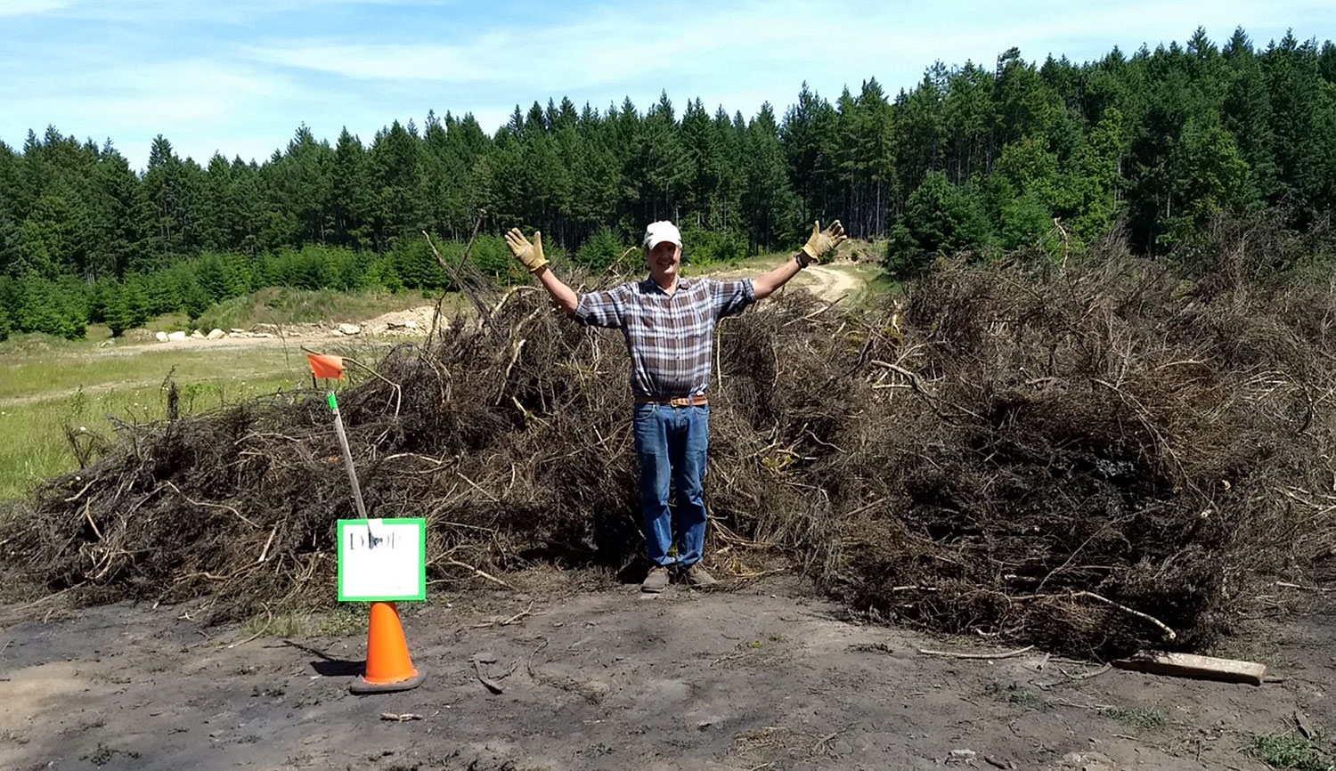 Person gesturing proudly in front of a big pile of broom.