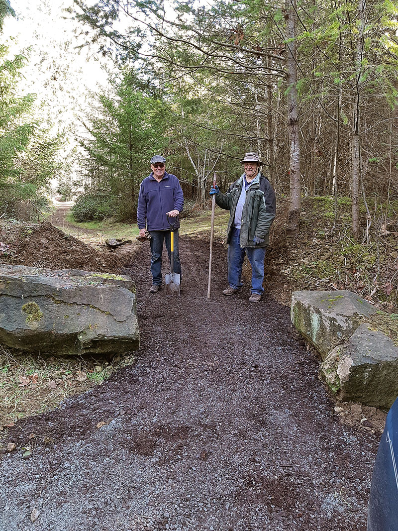 Two men with tools standing by an access path between big rocks.