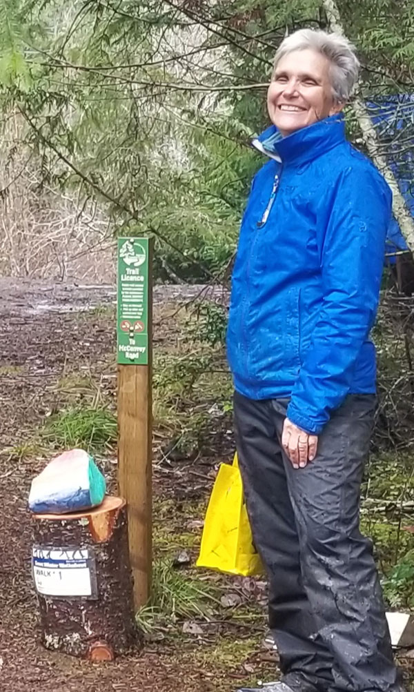 smiling woman standing by trail signpost