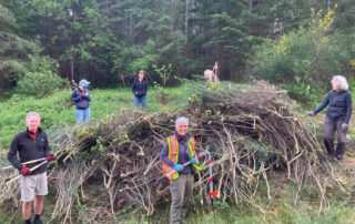 Group of socially distanced people standing around a big pile of broom.