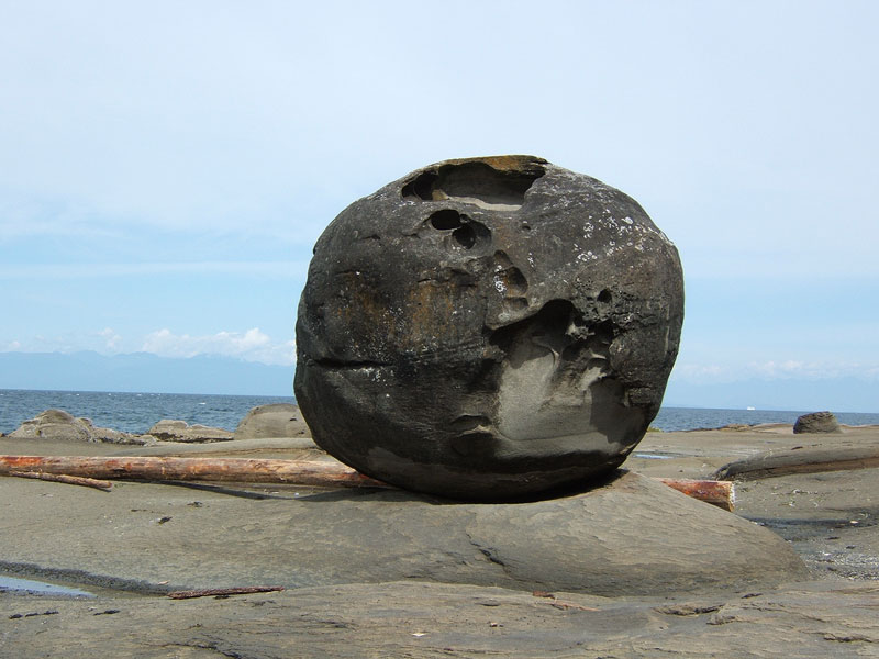 A large round boulder sitting on sandstone shelving.