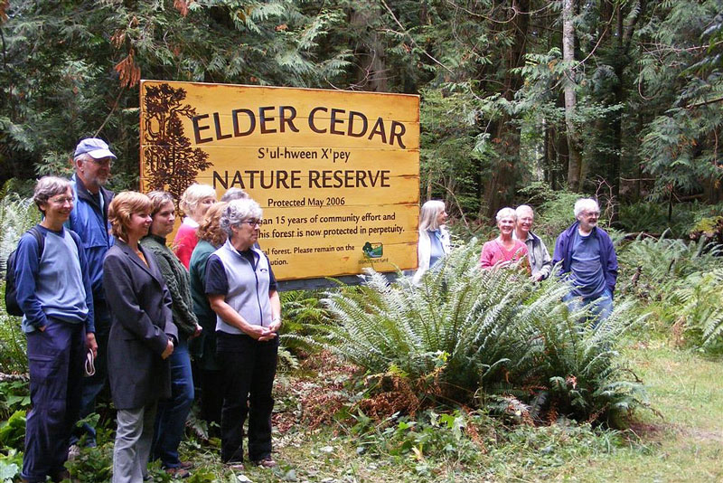 Group of people standing in front of a sign for the S'ul-hween X'pey (Elder Cedar) Nature Reserve.