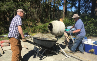 Two men pouring concrete into a wheelbarrow