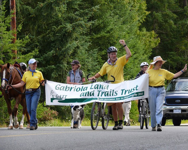 Group of people walking with a banner saying "Gabriola Land and Trails Trust."