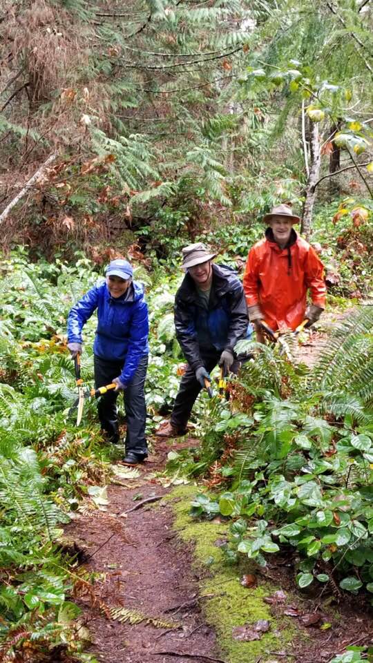 Group of cheerful people in rain trimming trail with loppers