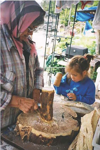 Indigenous woman and child pounding halibut with wooden tools.