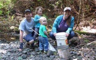 Adults and small children at a streamside with pails.
