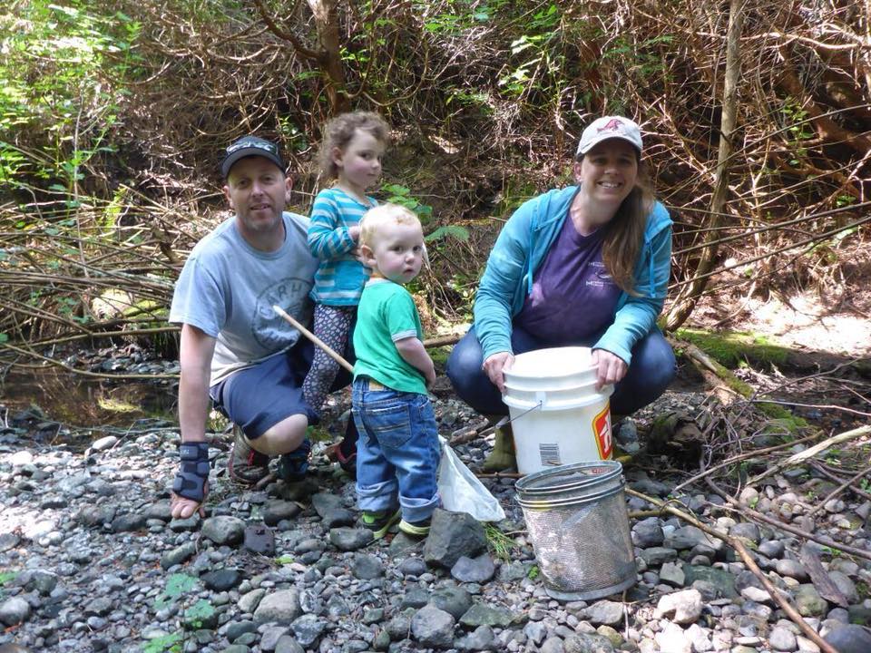 Adults and small children at a streamside with pails.