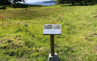 Photograph of a grassy meadow with string barriers and an interpretive sign explaining an ecological restoration project.