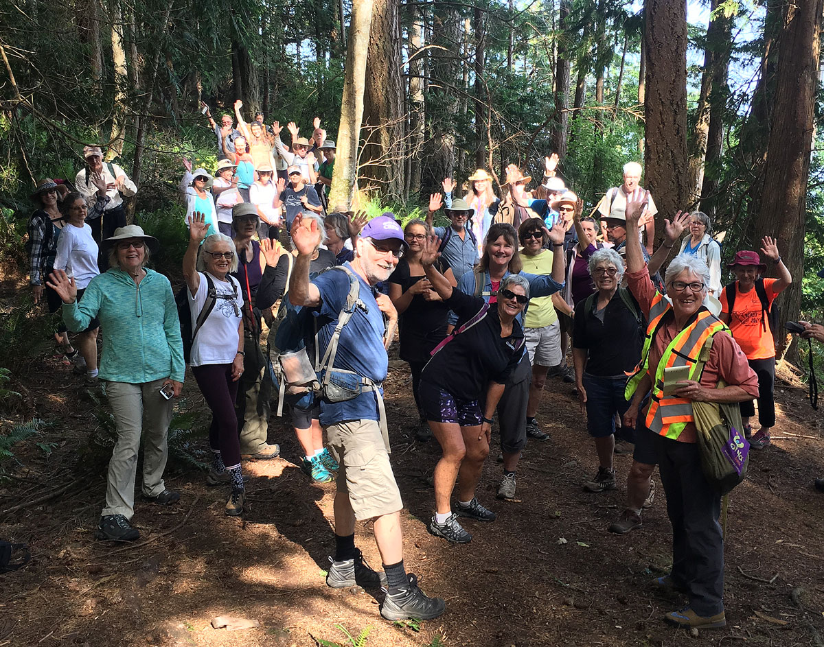 A large group of people on a trail, waving at the camera