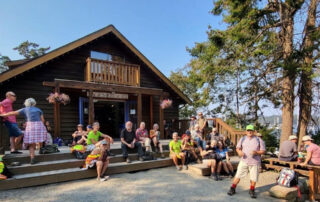 A tired but happy looking group of people sit on the steps and benches outside of a building. The sign on the building says "Page's Resort."