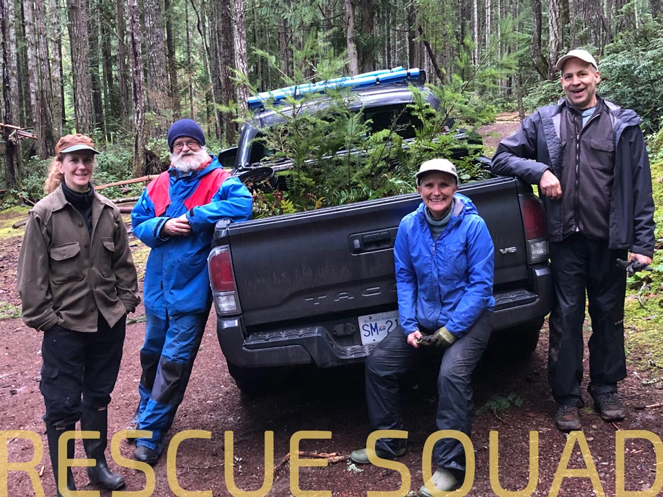A photo of happy people in front of a truck. The bed of the truck is full of small trees and plants. Text at the bottom of the photo says, "rescue squad."