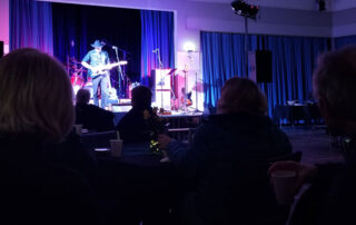 A guitar player stands onstage in front of an audience.