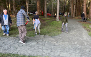 A crew of people work spreading gravel for an accessible pathway in a park.