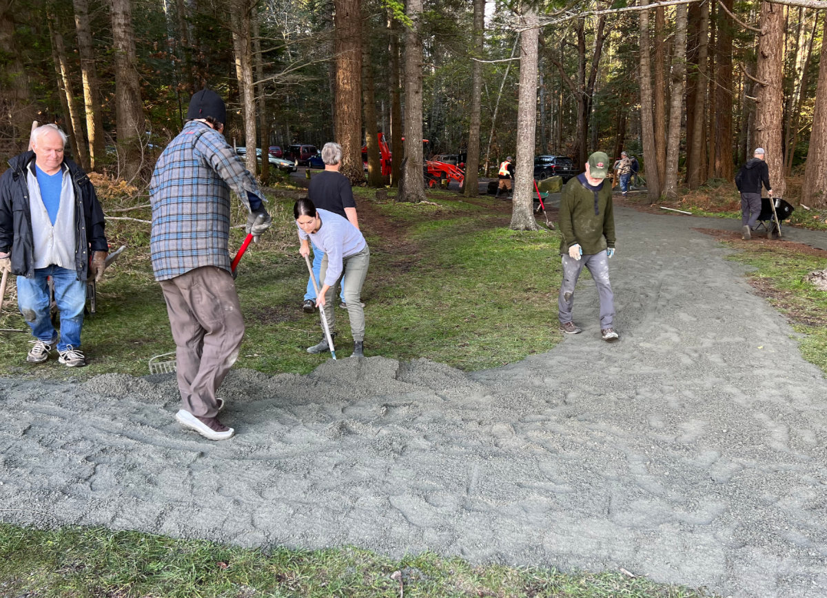 A crew of people work spreading gravel for an accessible pathway in a park.