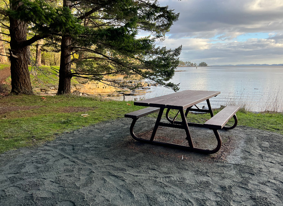 A picnic table sits on a bluff above the ocean looking out over a beautiful view. The ground by the table is freshly graveled.