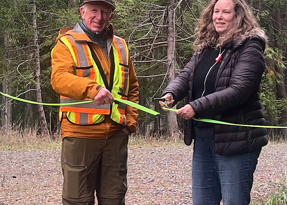 A man holds a ribbon for a woman to cut in an opening ceremony for a trail.