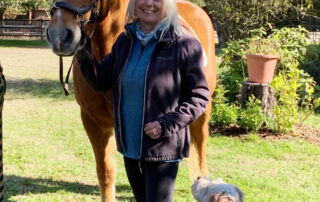 The photo shows a smiling woman standing with her horse and dog.