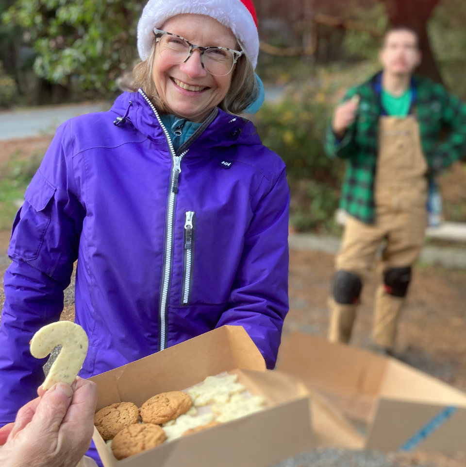 A smiling woman offers a box of cookies