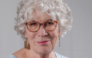 A headshot of a smiling woman with grey hair.