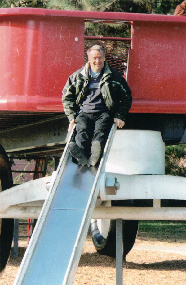 A grinning man sits at the top of a slide.