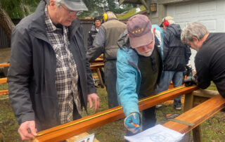 A group of people working to build frames for boardwalks. Those in front are measuring wood and checking plans.