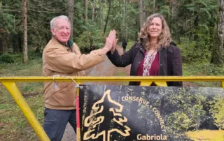 GaLTT president Hugh Skinner and RDN Director Vanessa Craig high-five each other in front of a gate on a trail into Wilkinson Woods.